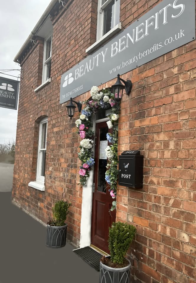 The front door of Beauty Benefits framed with a garland of flowers, under the Beauty Benefits sign