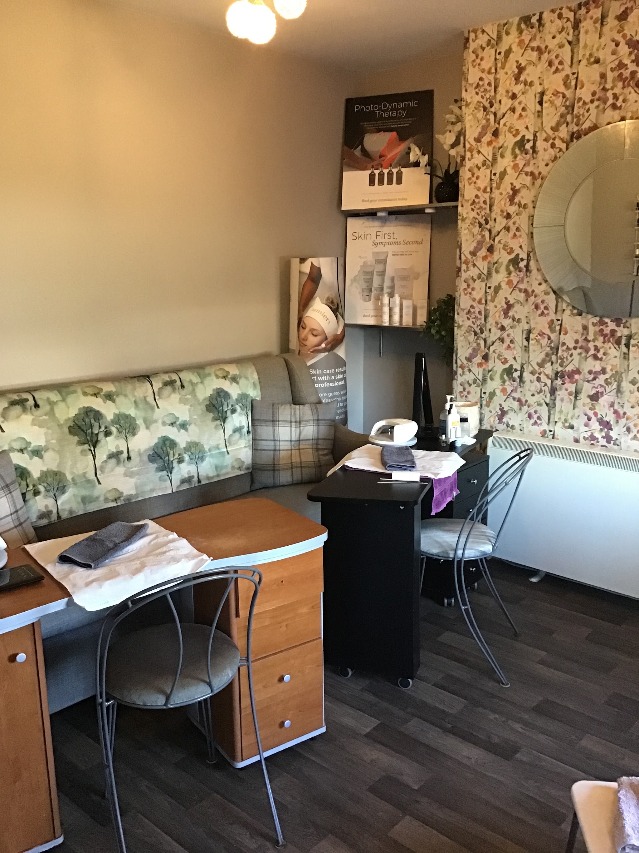A treatment room at Beauty Benefits with two manicure stations, a floral feature wall and a round mirror